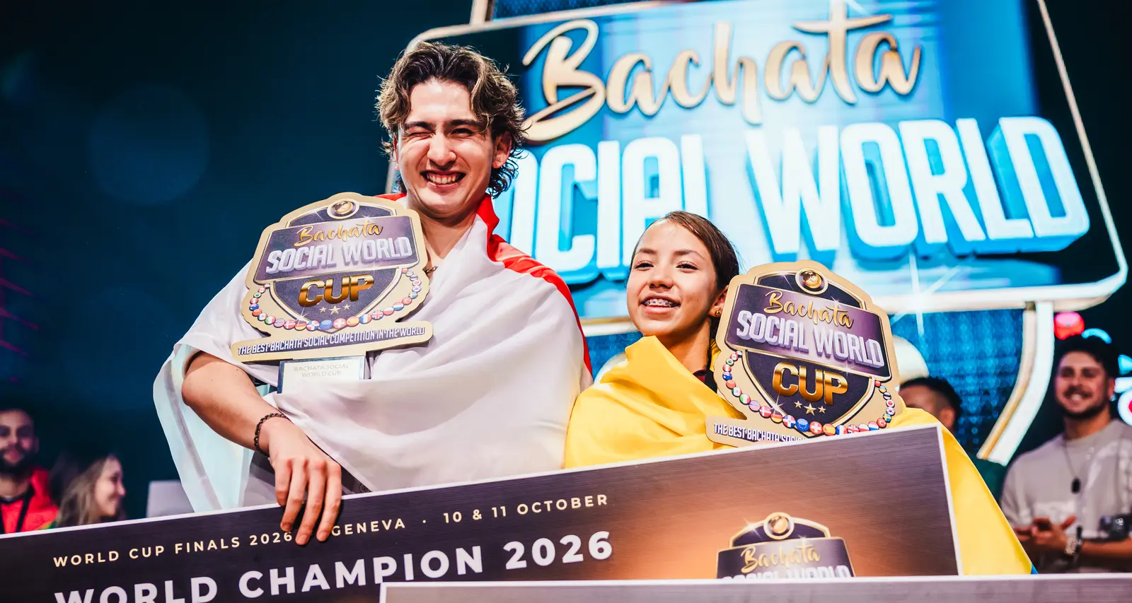 Victor Victor and Melany Mejia on stage in Geneva with their World Cup trophies and the World Champion 2026 cheques