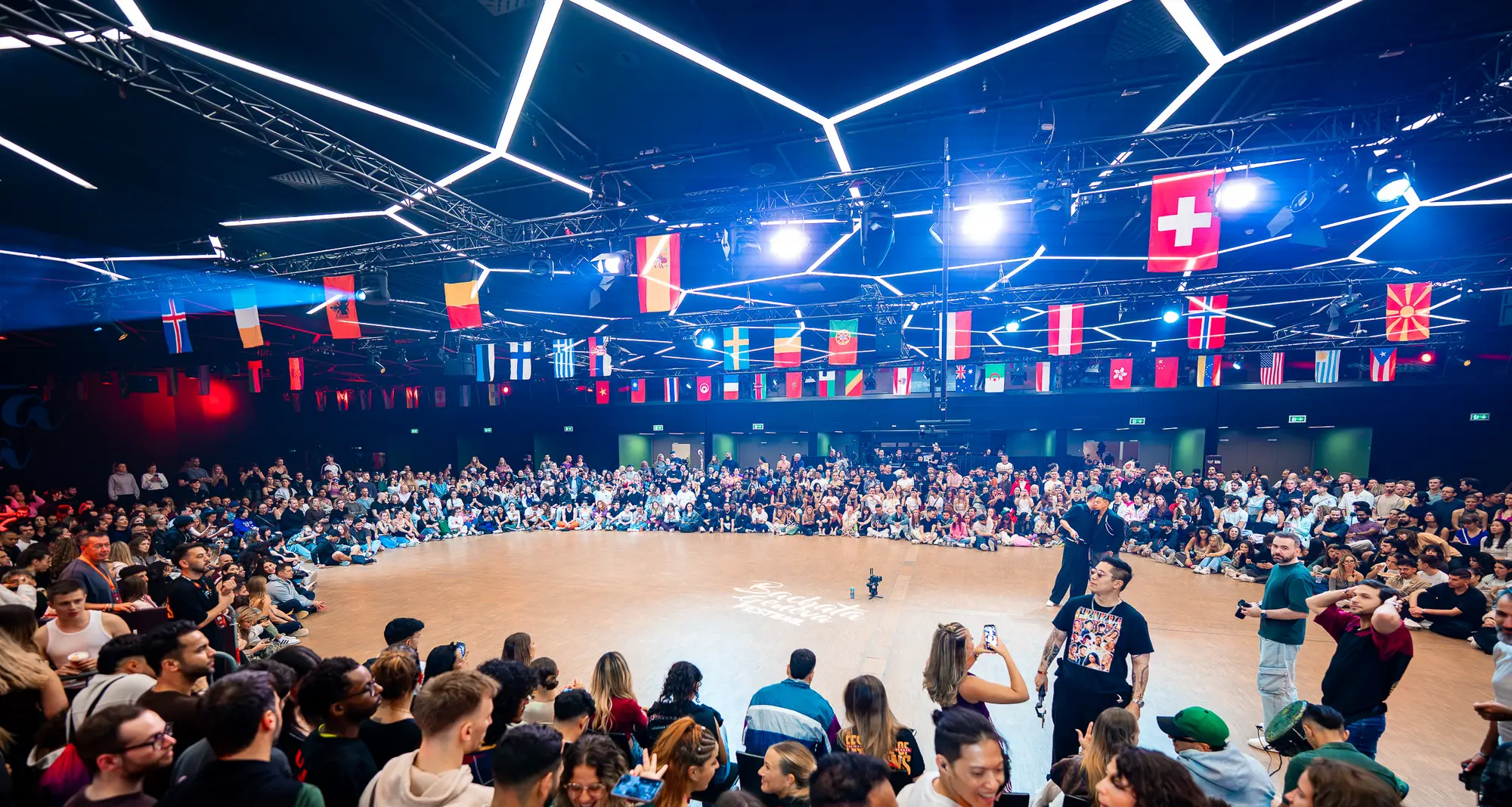The floor of the World Cup Finals 2026 in Geneva, dancers seated in a circle under the national flags